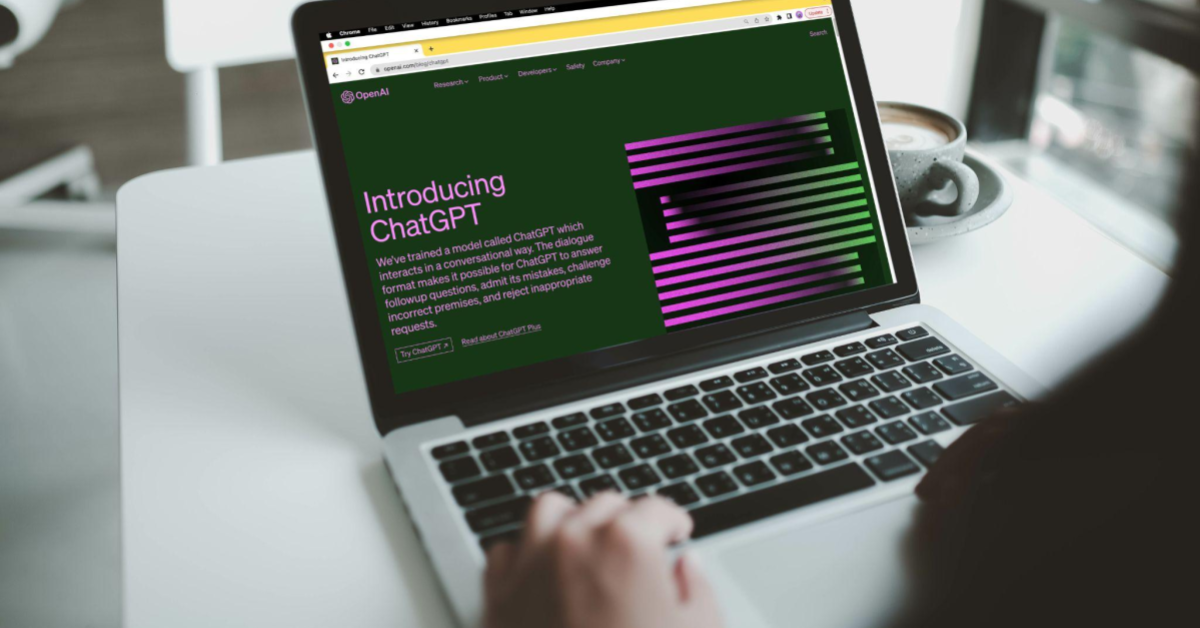 A imagem mostra um notebook em uma pessoa, enquanto um homem acessa a home page do ChatGPT. O homem não aparece na imagem, apenas sua mão e parte do ombro.
